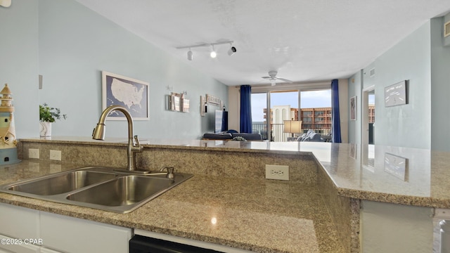 kitchen with light stone countertops, ceiling fan, a sink, track lighting, and open floor plan