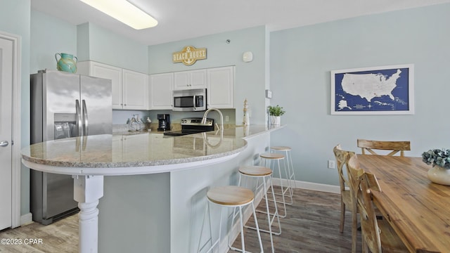 kitchen featuring a breakfast bar area, light stone counters, a peninsula, appliances with stainless steel finishes, and white cabinetry