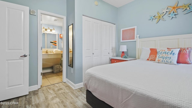 bedroom with a closet, ensuite bath, light wood-type flooring, and baseboards