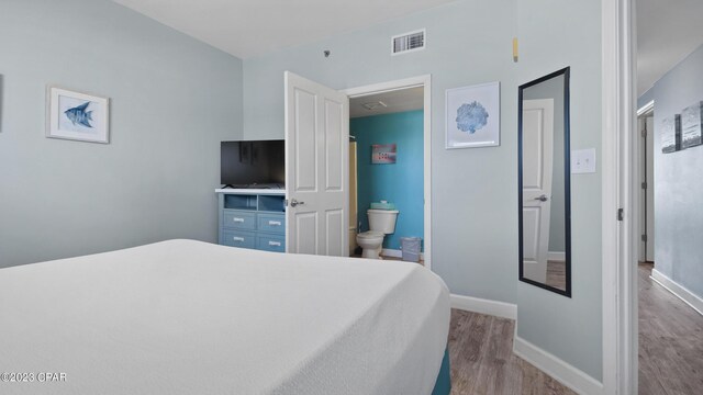 bedroom featuring ensuite bath, wood finished floors, visible vents, and baseboards