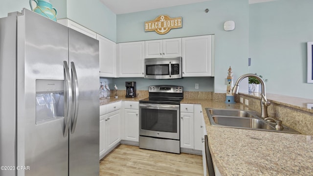 kitchen with light wood finished floors, a sink, stainless steel appliances, light countertops, and white cabinetry