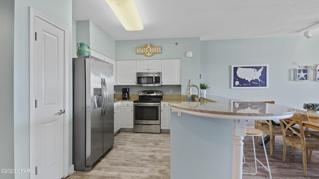 kitchen with white cabinets, appliances with stainless steel finishes, a kitchen bar, and a peninsula