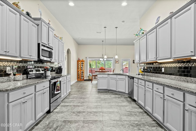 116 Lake Merial Blvd, Panama City, FL 32409 - kitchen with appliances with stainless steel finishes, a peninsula, gray cabinetry, decorative backsplash, and arched walkways
