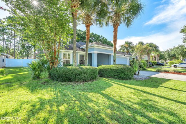 view of front of house featuring a front lawn, concrete driveway, an attached garage, and fence