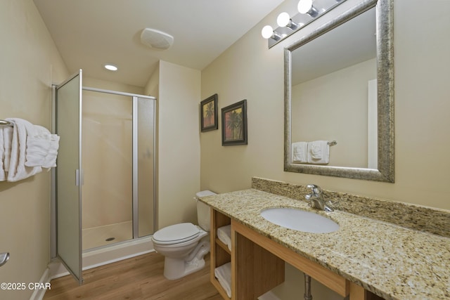 bathroom featuring wood finished floors, a stall shower, toilet, vanity, and recessed lighting