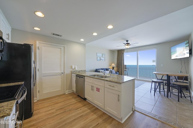kitchen with stainless steel appliances, a peninsula, white cabinets, a ceiling fan, and light stone counters