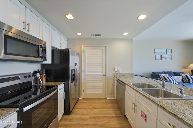 kitchen featuring stainless steel appliances, a sink, open floor plan, light wood-style flooring, and recessed lighting