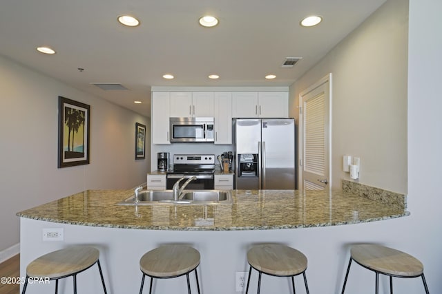 kitchen with appliances with stainless steel finishes, a sink, a kitchen bar, recessed lighting, and white cabinetry