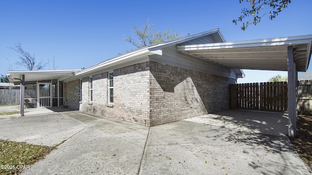 view of home's exterior with a carport, concrete driveway, fence, and brick siding