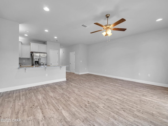 unfurnished living room featuring visible vents, baseboards, light wood-style floors, and a ceiling fan
