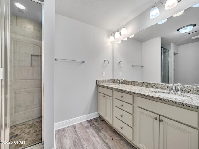 bathroom featuring a stall shower, a sink, wood finished floors, double vanity, and baseboards