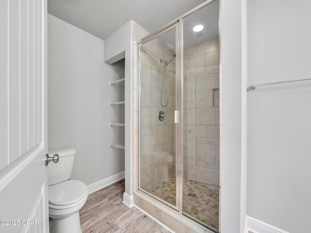 full bath featuring baseboards, wood finished floors, toilet, and a stall shower