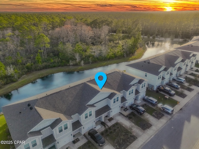 aerial view at dusk featuring a wooded view and a water view