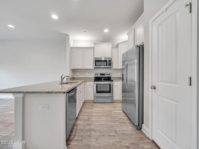 kitchen with light stone countertops, a peninsula, a sink, stainless steel appliances, and light wood-type flooring