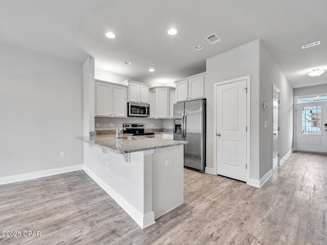 kitchen with light stone counters, a peninsula, a sink, light wood-style floors, and appliances with stainless steel finishes