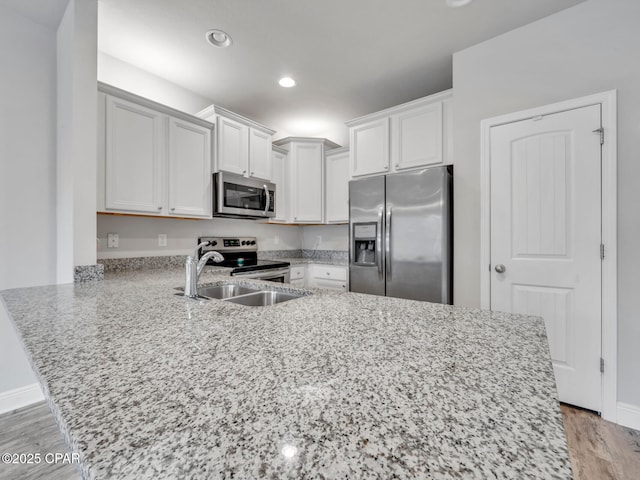 kitchen with white cabinetry, a peninsula, light wood finished floors, and appliances with stainless steel finishes