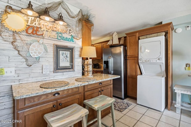8743 Thomas Dr Unit 225, Panama City Beach, FL 32408 - kitchen featuring stacked washer / drying machine, stainless steel refrigerator with ice dispenser, brown cabinetry, and light tile patterned floors