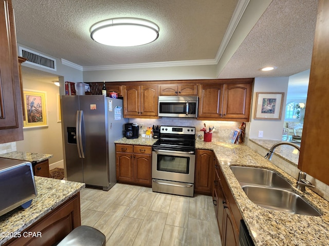 7205 Thomas Dr Unit E706, Panama City, FL 32408 - kitchen featuring appliances with stainless steel finishes, a sink, a textured ceiling, light stone counters, and brown cabinetry