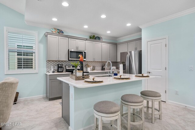 kitchen with a kitchen breakfast bar, crown molding, gray cabinetry, a sink, and stainless steel appliances