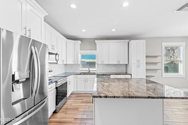 kitchen with stainless steel appliances, dark stone counters, a kitchen island, a sink, and visible vents