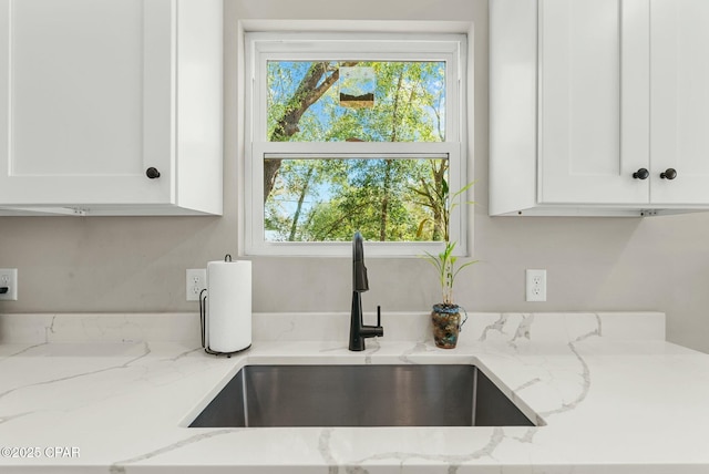 interior details with white cabinetry, a sink, and light stone counters