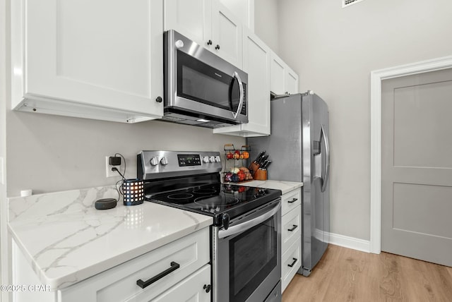 kitchen with light wood finished floors, white cabinetry, light stone countertops, and appliances with stainless steel finishes