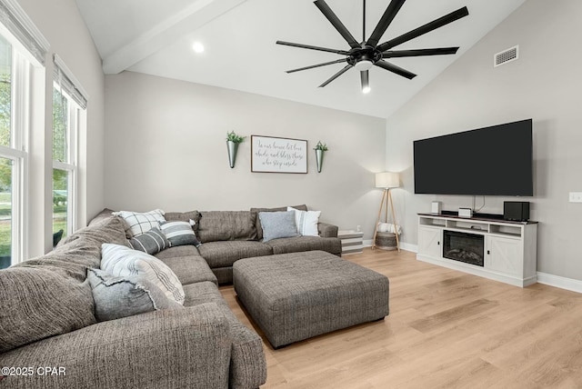living room featuring light wood-style flooring, visible vents, baseboards, a ceiling fan, and a glass covered fireplace