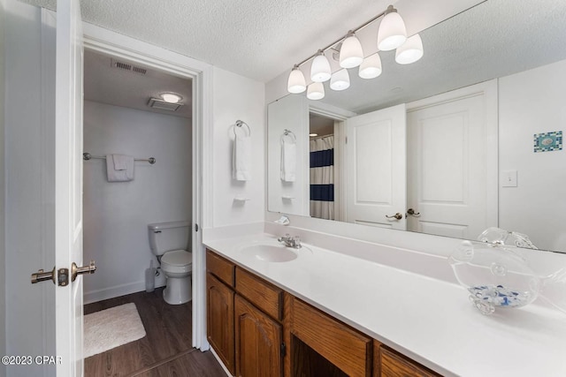 bathroom featuring a textured ceiling, visible vents, toilet, wood finished floors, and vanity