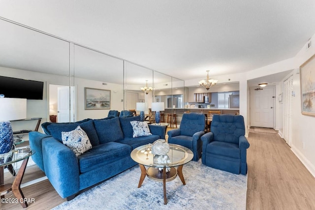 living area featuring baseboards, a textured ceiling, a notable chandelier, and light wood finished floors