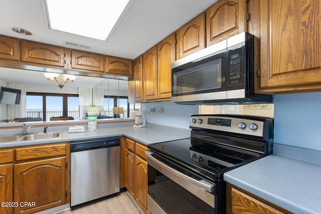 kitchen with light countertops, a chandelier, brown cabinets, stainless steel appliances, and a sink