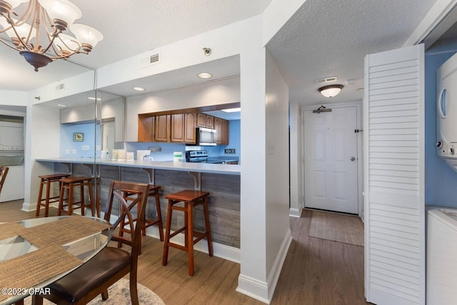 kitchen featuring visible vents, stacked washer / dryer, wood finished floors, brown cabinets, and appliances with stainless steel finishes