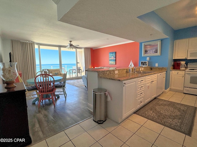kitchen featuring a ceiling fan, light tile patterned floors, a peninsula, stone counters, and white appliances