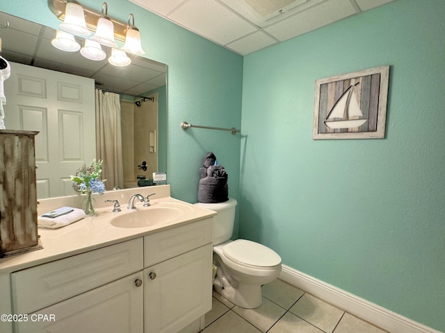 full bath with vanity, toilet, baseboards, a drop ceiling, and tile patterned floors