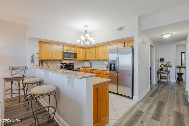 kitchen featuring stainless steel appliances, a chandelier, decorative backsplash, visible vents, and a peninsula