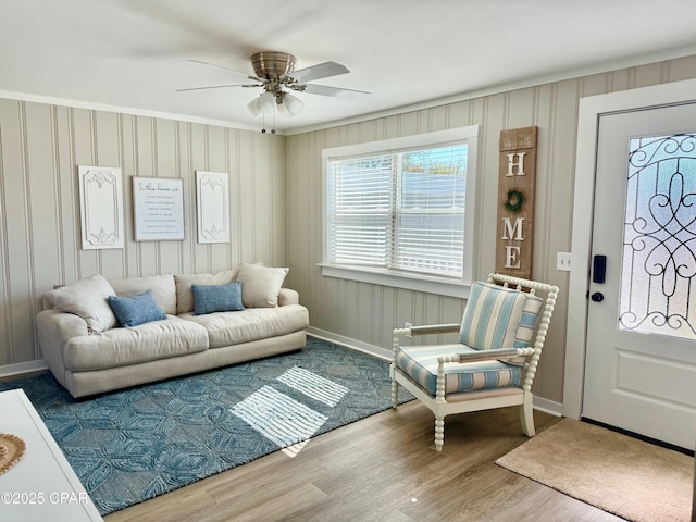 living area featuring wood finished floors, ornamental molding, baseboards, and a ceiling fan