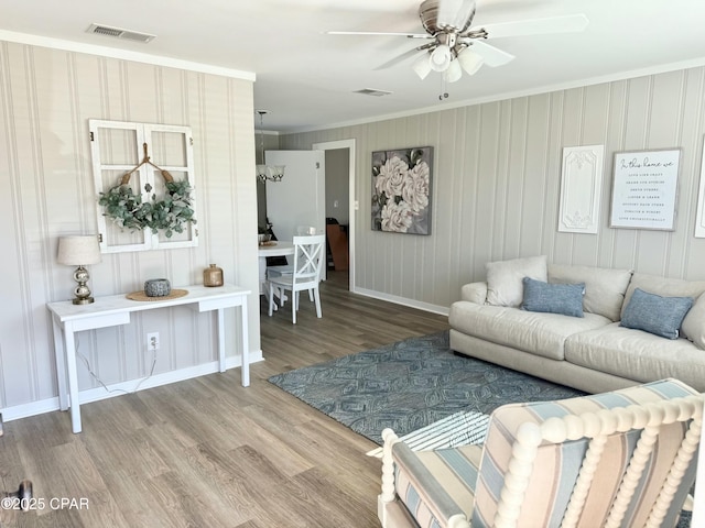 living area with baseboards, ornamental molding, visible vents, ceiling fan, and wood finished floors