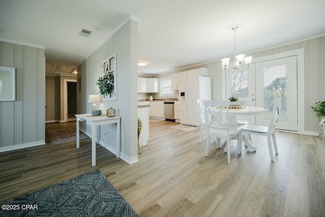 dining area featuring visible vents, a notable chandelier, a decorative wall, crown molding, and light wood finished floors