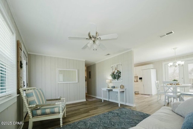 living room with light wood-style floors, visible vents, ceiling fan with notable chandelier, and crown molding