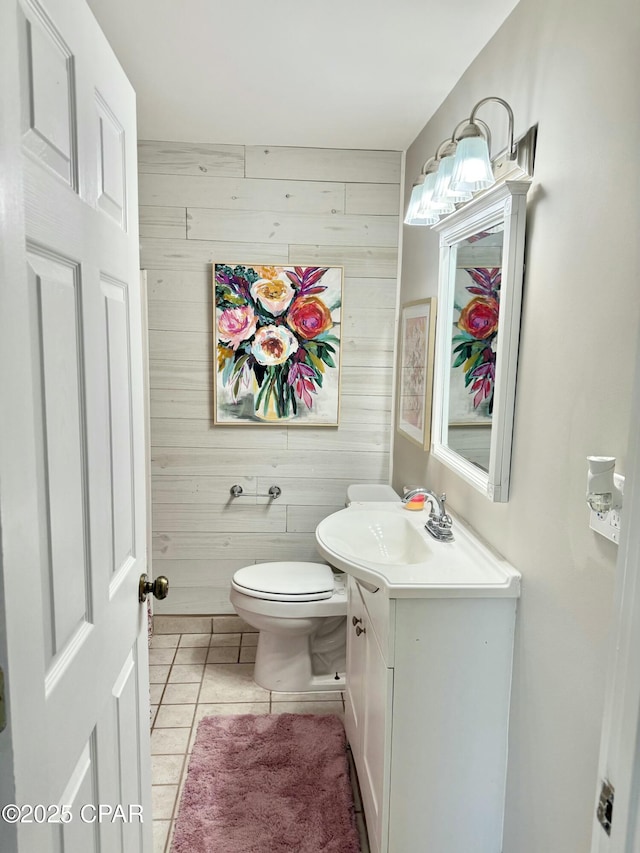 bathroom with toilet, tile patterned floors, wooden walls, and vanity