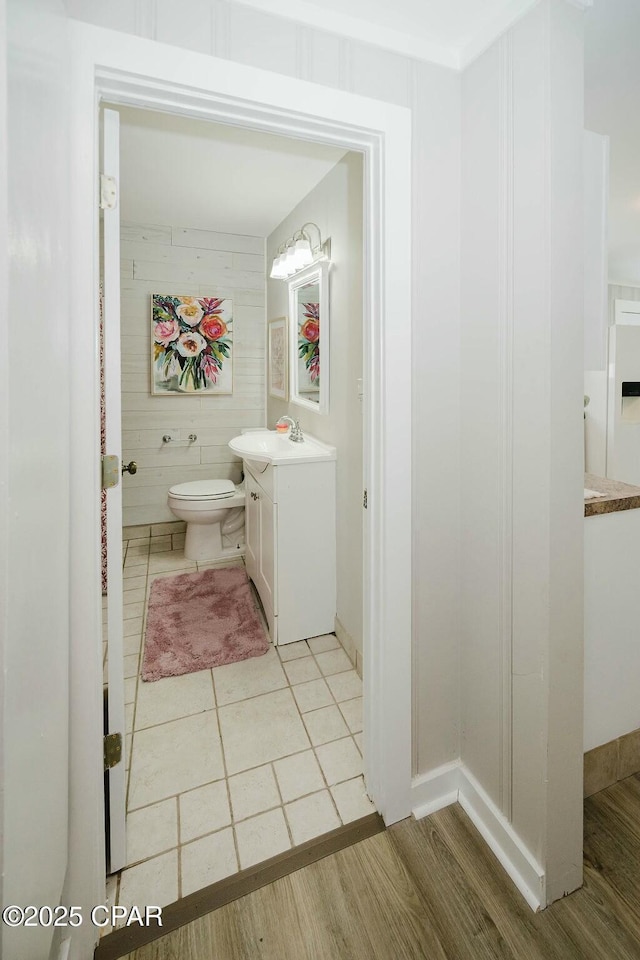 bathroom featuring baseboards, toilet, vanity, wood finished floors, and wood walls