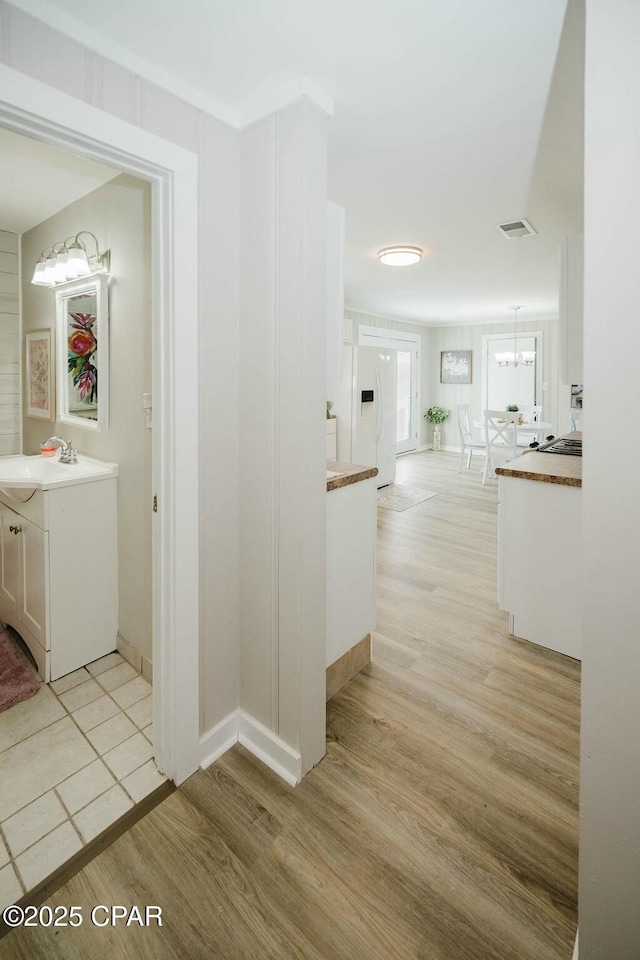 hall featuring a chandelier, light wood finished floors, a sink, and baseboards