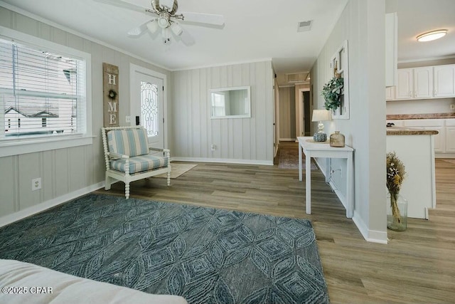 living area featuring baseboards, crown molding, light wood-style floors, visible vents, and ceiling fan