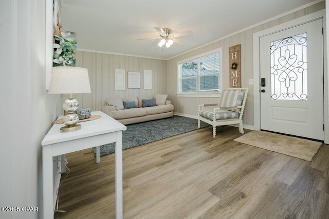living room with a ceiling fan, wood finished floors, baseboards, and ornamental molding