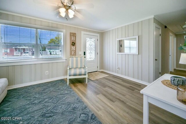 foyer entrance featuring baseboards, a ceiling fan, crown molding, and wood finished floors