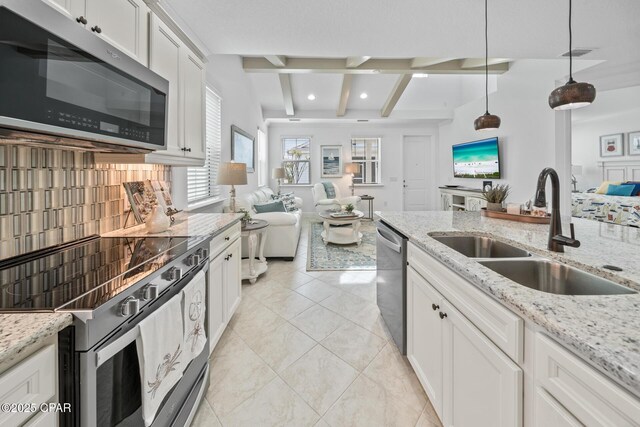 kitchen featuring beam ceiling, a sink, white cabinetry, open floor plan, and stainless steel appliances