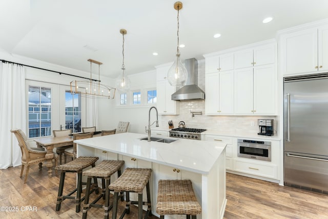 kitchen with tasteful backsplash, wood finished floors, appliances with stainless steel finishes, a sink, and wall chimney exhaust hood
