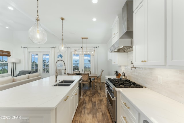 kitchen with wall chimney range hood, a sink, stainless steel appliances, dark wood finished floors, and backsplash