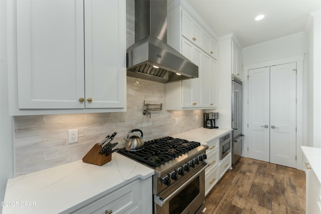 kitchen with light stone counters, crown molding, white cabinets, premium appliances, and wall chimney exhaust hood