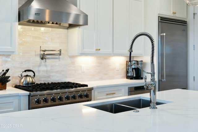 kitchen featuring stove, stainless steel built in refrigerator, white cabinetry, and wall chimney range hood