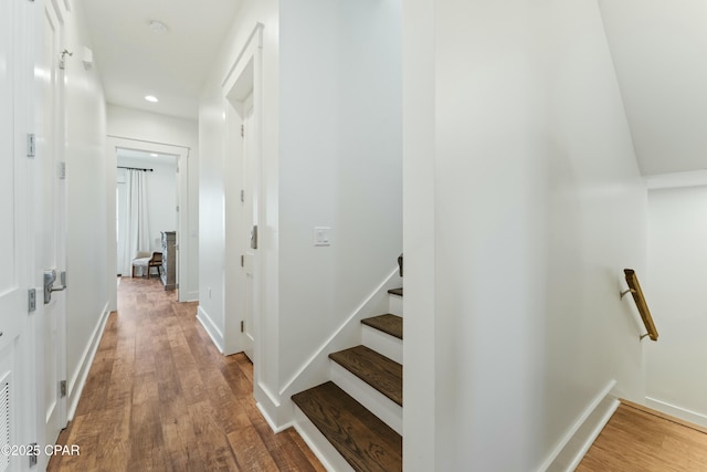 corridor featuring baseboards, recessed lighting, wood finished floors, and an upstairs landing